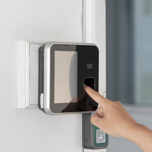A person using a fingerprint scanner on a wall-mounted access control device.