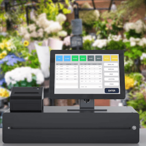 Point of Sale (POS) system setup in a flower shop with a blurred background of colorful flowers and greenery.