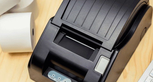 Compact black barcode printer on a wooden desk.