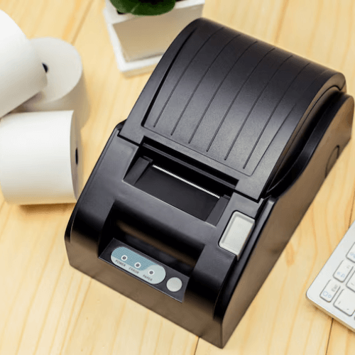 Compact black barcode printer on a wooden desk.