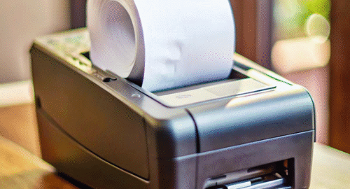 A receipt printer with a roll of paper on a wooden surface.
